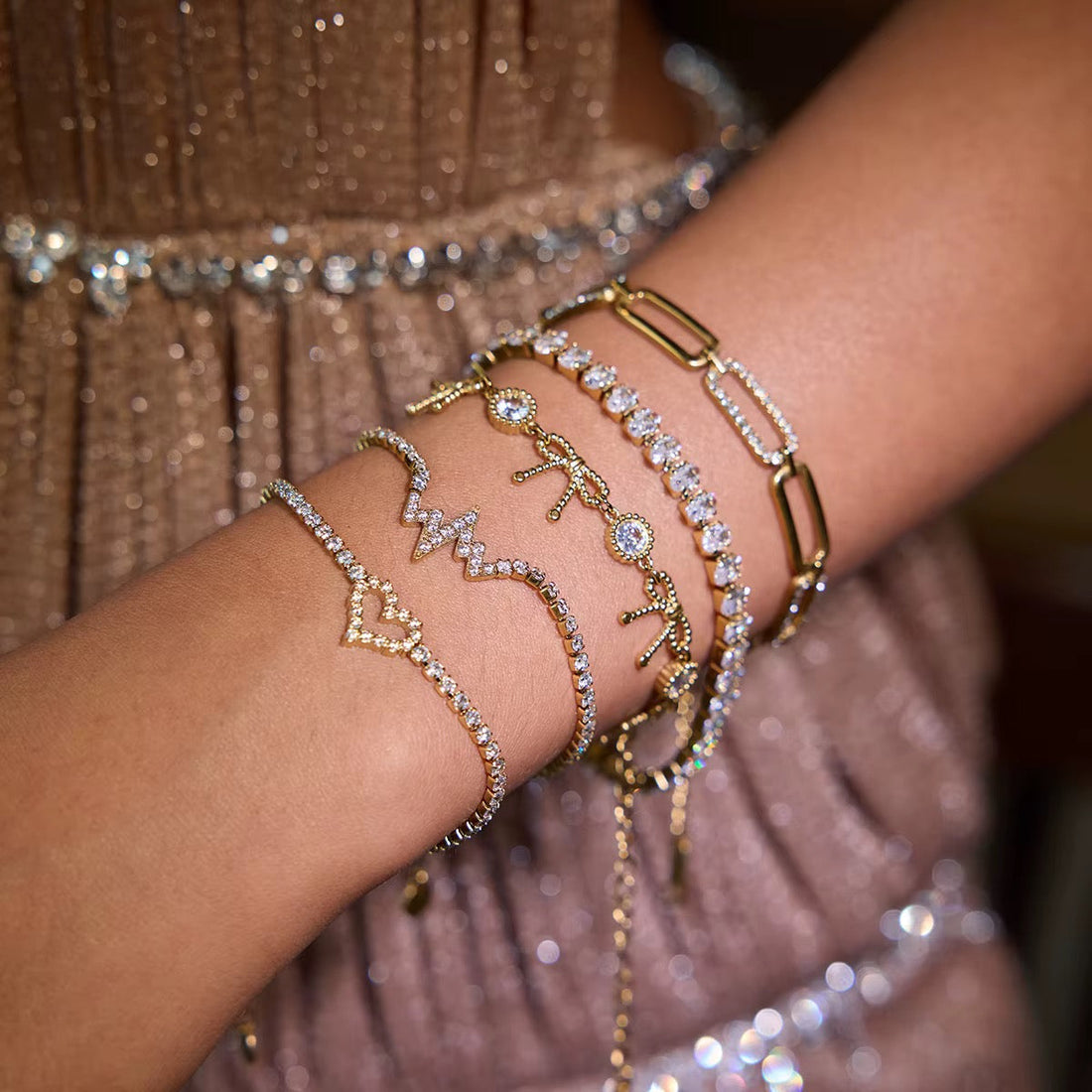 Mano con varias pulseras y cadenas chapadas en oro de Kapri Gold apiladas en la muñeca